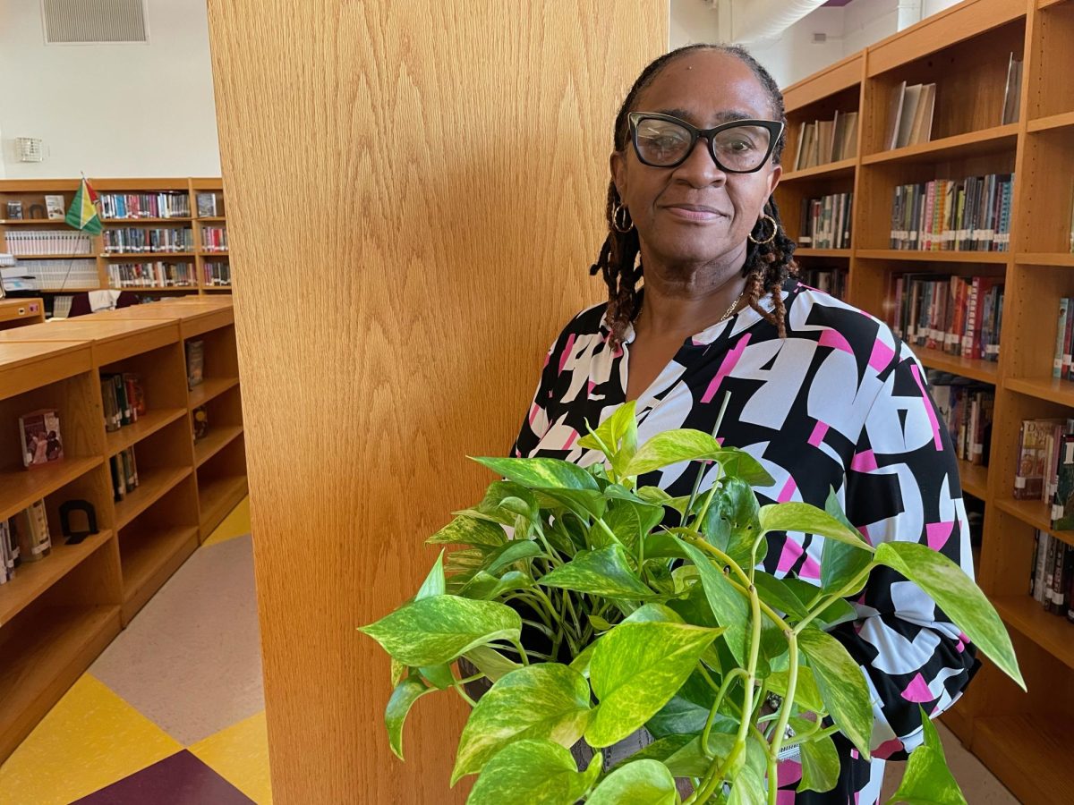 Ms. Cameron poses with one of her beloved plants in the library. 